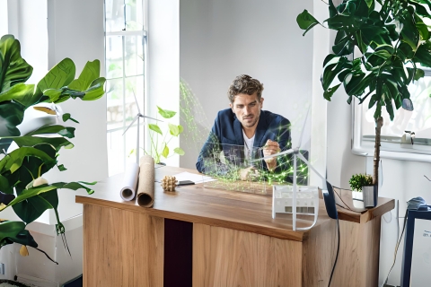 man inspecting at desk with wind farms and green energy objects around him inspecting data
